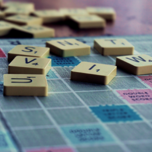 Close up photo of Scrabble game board, scattered scrabble game pieces, letters U, V, I, S, N, T, W