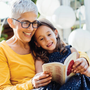 grandmother sitting with grand-daughter, reading a small book